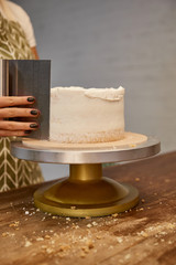 Cropped view of confectioner aligning sweet cream on biscuit on stand