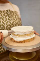 Cropped view of confectioner with pastry bag adding cream on biscuit on stand isolated on grey