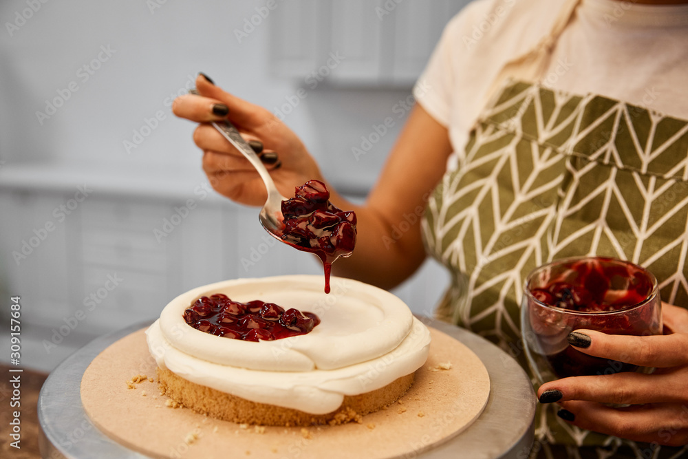 Wall mural cropped view of confectioner adding tasty berry jam on cake