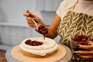 Cropped view of confectioner adding tasty berry jam on cake