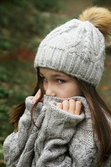  winter portrait of a beautiful girl covering her face with a woolen scarf. Closeup of a girl feeling cold outdoor in the city. Young girl holding a scarf and looking at camera.