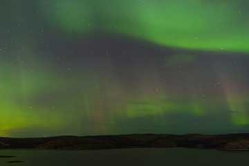 Northern lights over the lake and hills. Aurora at night in the sky in the north.