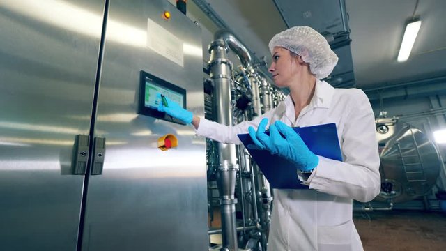 Plant worker checks a machine, typing on display. Female worker controls the quality of production equipment.