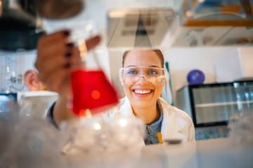 Young woman working with liquids in glassware. Young chemist looking at flask with fluid substance in lab. Scientist Working in The Laboratory.  Student of chemistry working in laboratory