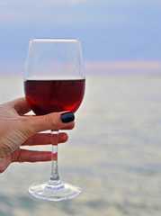 Female hand holds a wine glass on sea background.