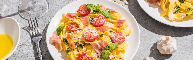 fresh Pappardelle with tomatoes, pesto and prosciutto near ingredients on grey surface, panoramic shot