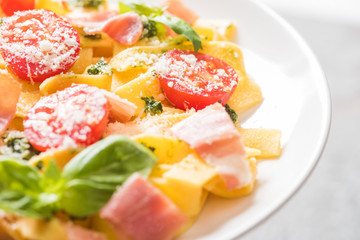 close up view of delicious Pappardelle with tomatoes, Parmesan, pesto sauce, basil and prosciutto