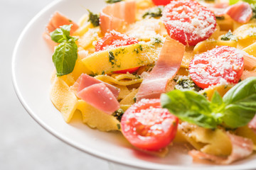 close up view of delicious Pappardelle with tomatoes, Parmesan, pesto sauce, basil and prosciutto