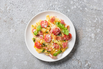 top view of cooked Pappardelle with tomatoes, pesto sauce and prosciutto on grey surface