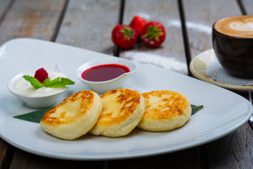 Traditional breakfast with coffee and cheesecakes, cottage cheese pancakes on a plate with syrup and jam.