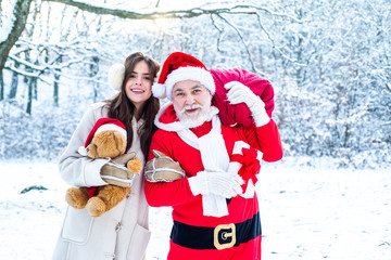 Santa with winter girl in red suit walking along the road to Christmas. Santa Claus and snow girl in red costume walk in winter forest.