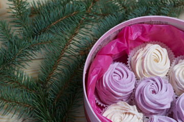 Homemade marshmallows in a round box. Decorated with fir branches. On pine boards. View from above.