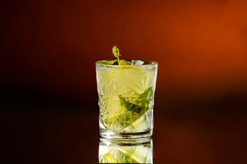 A glass full of an alcoholic Mojito from sour lime, rum, mint and ice cubes on a dark