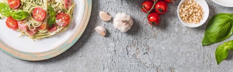 top view of cooked Pappardelle with tomatoes, basil and prosciutto near ingredients on grey surface, panoramic shot