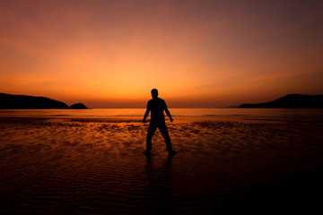 Fototapeta premium Silhouette action of a young man fun under twilight sunset sky at sea beach.