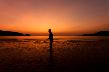 Fototapeta na wymiar Silhouette action of a young man fun under twilight sunset sky at sea beach.