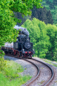 Alte Dampflok mit Waggons in einer Kurve vor B&auml;umen.