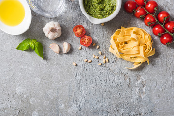 top view of raw Pappardelle near tomatoes, garlic, basil, pine nuts, olive oil, water and pesto...