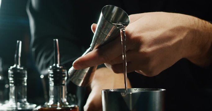 Close up of a professional bartender is preparing an alcoholic cocktail with ice cubes to customers at the bar or disco club.