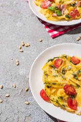 tasty Pappardelle with tomatoes, pesto and prosciutto with fork near red wine, basil and pine nuts on grey surface