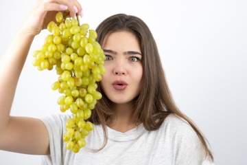 young beautiful surprised woman standing with bunch of green grapes standing on isolated white background dietology and nutrition