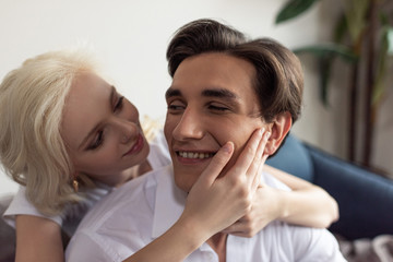 Smiling blonde girl touching boyfriend face at home