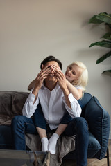 Smiling young girl covering boyfriend eyes with hands on sofa in living room