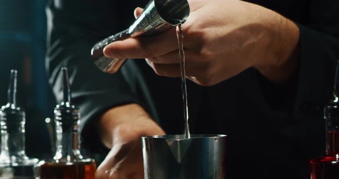 Close up of a professional bartender is preparing an alcoholic cocktail with ice cubes to customers at the bar or disco club.