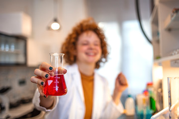 A female medical or scientific researcher or woman doctor looking at a test tube of clear solution in a laboratory with her microscope beside her. Young female geneticists looking in sample