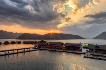Obraz premium Tourists relaxing on wooden raft resort floating on Srinakarin dam in evening