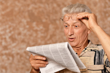 Close-up portrait of senior man reading newspaper on a beige background