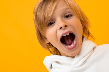 cute blond boy screams on a yellow studio background close-up