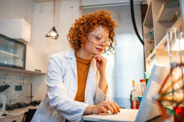 Working in lab. Portrait of confident female scientist working on laptop in chemical laboratory....
