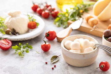 Italian cheeses burrata, mozzarella, scorocia, boccini with olives, cherry tomatoes and arugula on a round white plate on a light background.