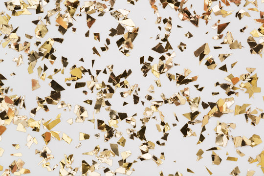 Gold leaf confetti on white background. Festive, party or holiday glitter backdrop. Flat-lay, close-up.
