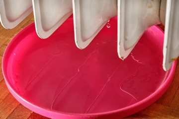 Old white leaking radiator in a living room with parquet floor and a pink plastic bowl ( turned...