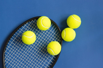 Tennis balls and black racket on blue background. Color of the year 2020, horizontal format photo. Active lifestyle concept. Sports equipment, top view