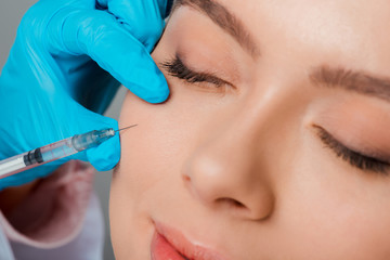 close up of beautician in latex glove holding syringe near girl with closed eyes