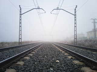 Train tracks and catenary posts disappear into thick fog