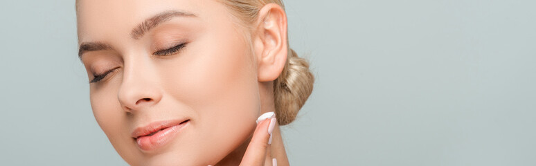 panoramic shot of happy woman applying face cream isolated on grey