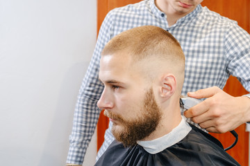 Barber hands shaves the client's head with trimmer, selective focus