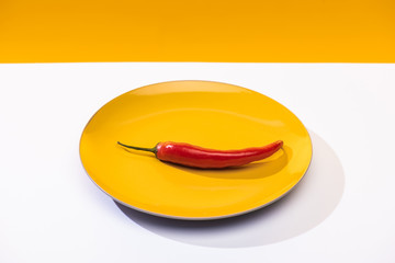 Spicy chili pepper on plate on white surface on yellow background