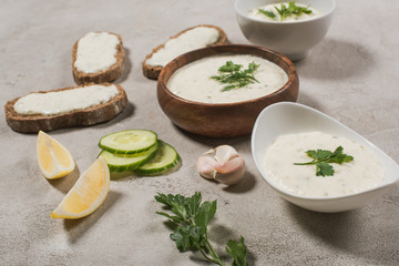 Tzatziki sauce in bowls with raw ingredients on stone background