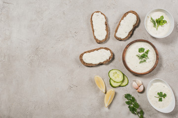 Top view of homemade tzatziki sauce with bread and ingredients on stone background