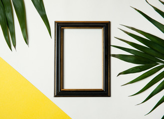 Travel and vacation concept. Photo frame framed with green tropical leaves on a yellow white  background. 
