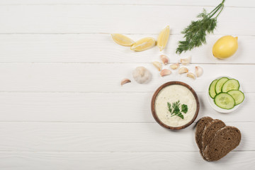Top view of tzatziki sauce with ingredients and bread on white wooden background