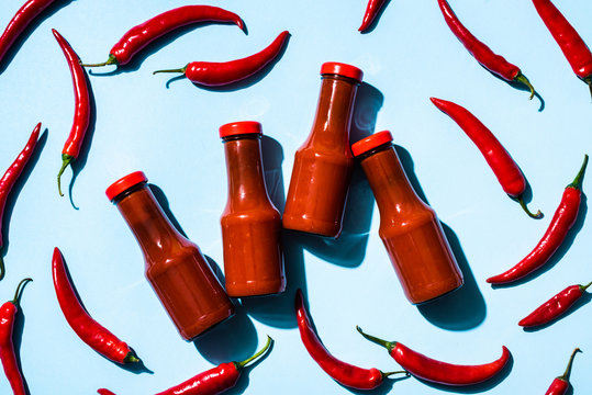 Top view of bottles with homemade chili sauce and chili peppers on blue background