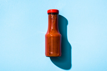 Top view of bottle with ketchup on blue background