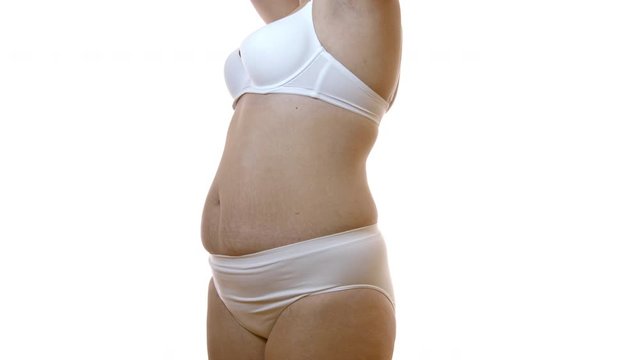 Closeup on flabby belly of female body with stretch marks over white studio background. Overweight woman wearing only white underwear presenting her skin and dermatology issues.