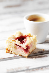 Piece of yeast cake and a cup of coffee on white wooden background. Close up. 